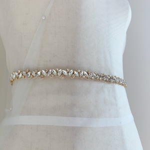 Puede incluir: Un cintur&oacute;n de novia dorado con adornos de cristal transparente. El cintur&oacute;n est&aacute; hecho de un material delgado y flexible y est&aacute; adornado con una fila de cristales brillantes.