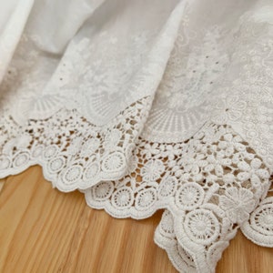 May include: White cotton fabric with a delicate lace trim. The lace features a scalloped edge and intricate floral designs.
