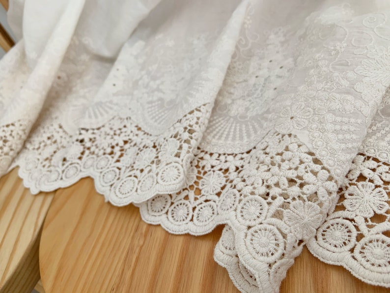 May include: White cotton fabric with a delicate lace trim. The lace features a scalloped edge and intricate floral designs.