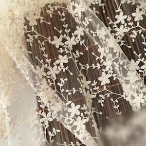May include: Close-up of ivory-colored lace fabric with a delicate floral pattern. The lace is sheer and has a soft, romantic feel.