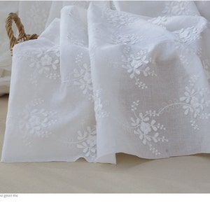 May include: White cotton fabric featuring delicate white embroidery of small floral designs. The fabric is soft and sheer, ideal for crafting or sewing projects.