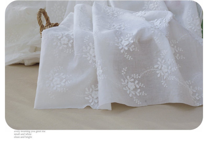 May include: White cotton fabric featuring delicate white embroidery of small floral designs. The fabric is soft and sheer, ideal for crafting or sewing projects.