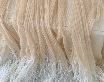 Puede incluir: Tela de tul beige con un ribete de plumas blancas. El tul tiene un brillo sutil y las plumas son suaves y esponjosas.