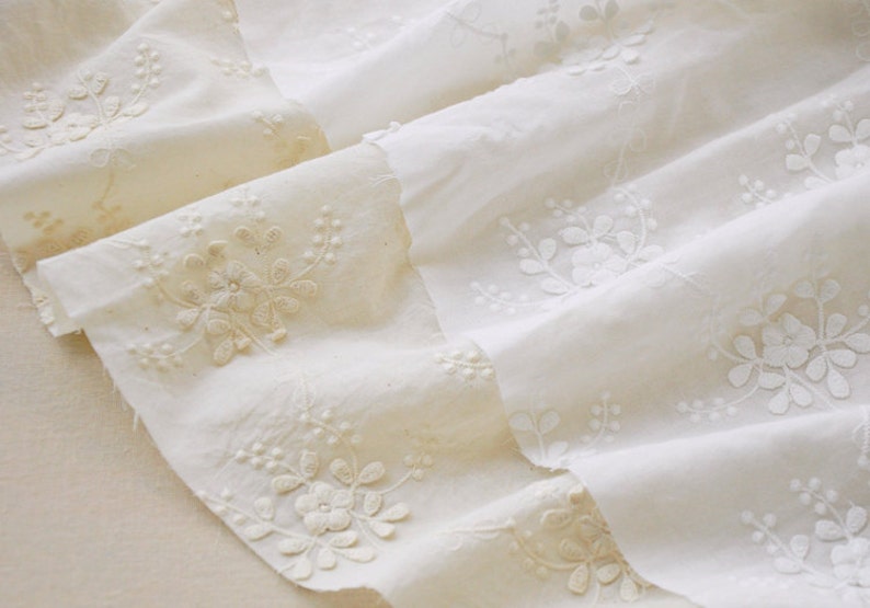May include: Two pieces of white cotton fabric with delicate floral embroidery. The fabric is layered and the embroidery is visible on both sides.