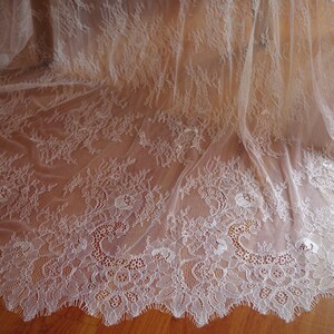 May include: White lace fabric with a delicate floral pattern. The lace has a scalloped edge and is sheer and lightweight.
