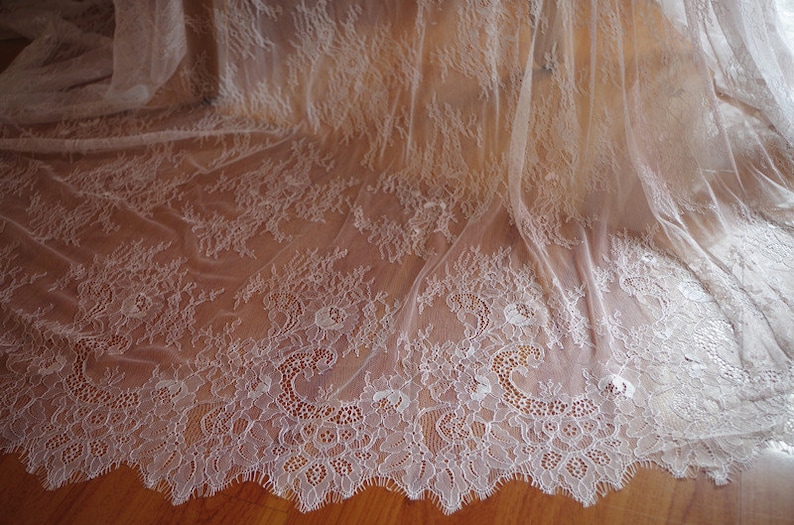 May include: White lace fabric with a delicate floral pattern. The lace has a scalloped edge and is sheer and lightweight.