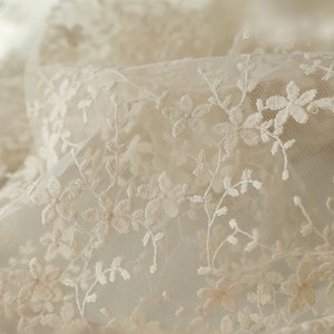 May include: White delicate lace fabric with a floral pattern. The lace is sheer and has a soft, romantic feel.