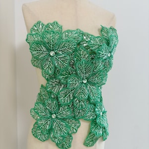 May include: Green beaded floral applique with sequins and rhinestones. This embellishment is perfect for adding a touch of sparkle and elegance to any garment.