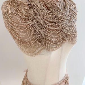 May include: A gold beaded choker necklace and matching skirt. The necklace is a wide, layered design with a fringe. The skirt is a high-waisted, layered design with a fringe.