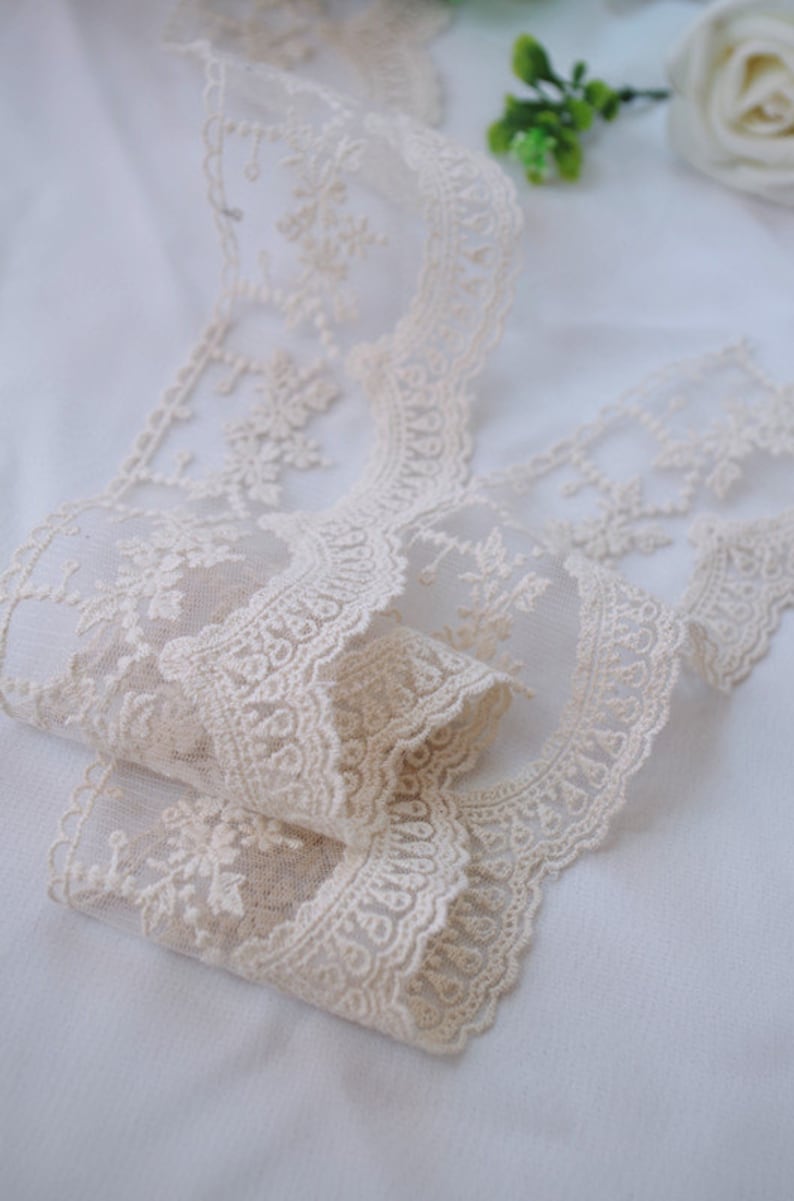 May include: A close-up of a beige lace trim with a delicate floral pattern. The lace is soft and flowing, with a subtle sheen.