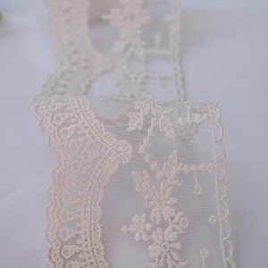 May include: Ivory lace trim with a delicate floral pattern. The lace is sheer and has a scalloped edge.