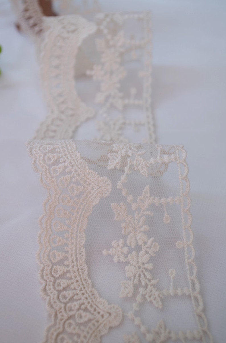 May include: Ivory lace trim with a delicate floral pattern. The lace is sheer and has a scalloped edge.