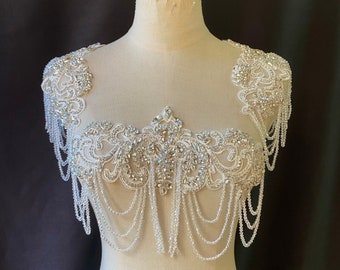 May include: A white beaded and rhinestone bridal shoulder piece with a delicate floral design. The piece features a cascading chain of beads and rhinestones.