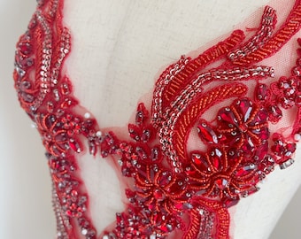 May include: Red beaded applique with a floral design. The applique is made with red beads, sequins, and rhinestones. It is perfect for adding a touch of sparkle to any garment.