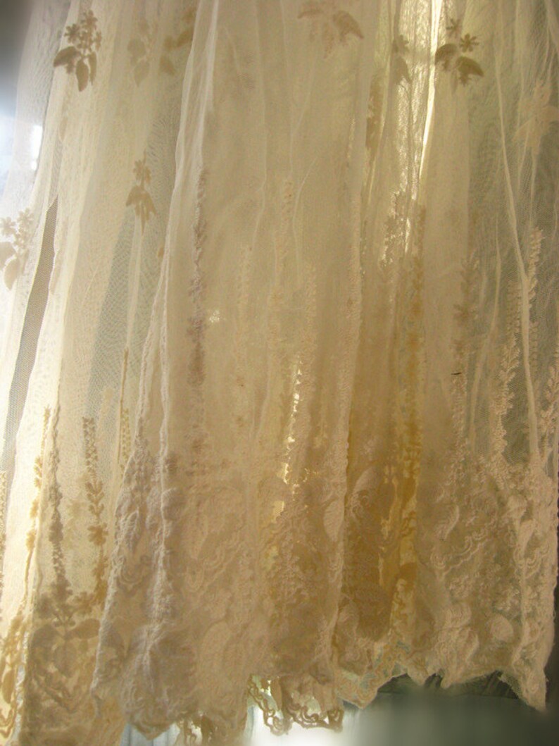 May include: White lace curtain with a delicate floral pattern. The curtain is sheer and translucent, allowing light to shine through.