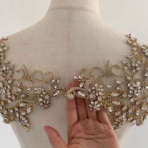 May include: A gold and clear crystal embellishment with a floral design. The embellishment is on a white background.