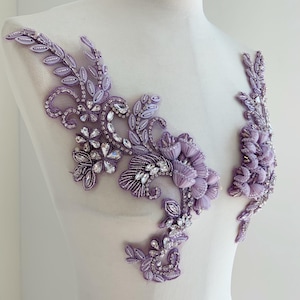 Puede incluir: Aplicación floral lavanda con intrincados abalorios y detalles de cristal. El diseño presenta hojas, flores y patrones arremolinados, creando un adorno delicado y ornamentado. La aplicación se muestra sobre un maniquí blanco.