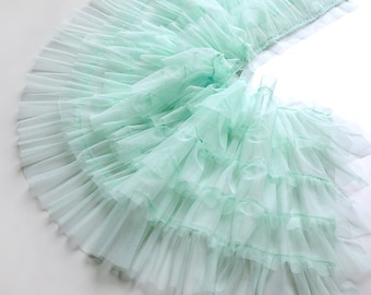 May include: A light green tulle fabric with multiple layers of ruffles. The fabric is soft and delicate, and it would be perfect for a variety of crafting projects.