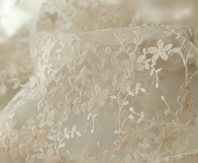 May include: White delicate lace fabric with a floral pattern. The lace is sheer and has a soft, romantic feel.