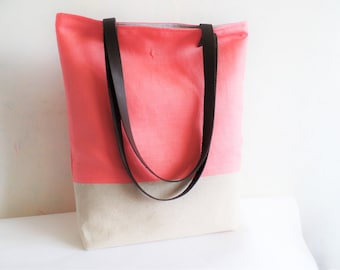 May include: A coral and beige tote bag with black leather straps. The bag is made of a canvas material.