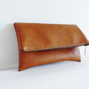 May include: A brown leather clutch purse with a zipper closure.