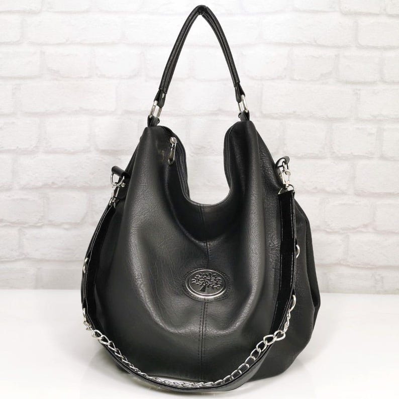 Peut inclure: Sac &agrave; bandouli&egrave;re noir avec une cha&icirc;ne argent&eacute;e et un embl&egrave;me d'arbre. Le sac a une forme arrondie avec une poign&eacute;e sup&eacute;rieure et une bandouli&egrave;re amovible. Le sac est fait d'un mat&eacute;riau lisse et mat.