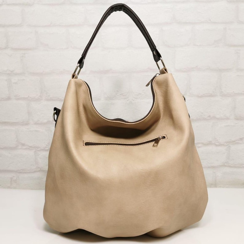 Peut inclure: Un sac hobo beige avec une poign&eacute;e et des bordures noires. Le sac poss&egrave;de une poche zipp&eacute;e &agrave; l'avant et un int&eacute;rieur spacieux. Fabriqu&eacute; dans un mat&eacute;riau doux et textur&eacute;, il est adapt&eacute; &agrave; un usage quotidien.