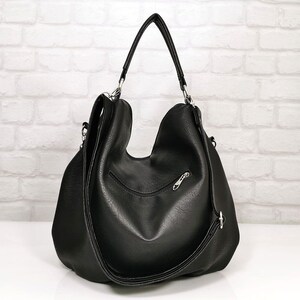 Peut inclure: Sac &agrave; bandouli&egrave;re noir avec un design incurv&eacute;. Le sac a une poign&eacute;e sup&eacute;rieure et une longue bandouli&egrave;re r&eacute;glable. Des &eacute;l&eacute;ments m&eacute;talliques argent&eacute;s ornent le sac, notamment la fermeture &eacute;clair et les attaches de la bandouli&egrave;re. Le sac est en mati&egrave;re lisse et mate.