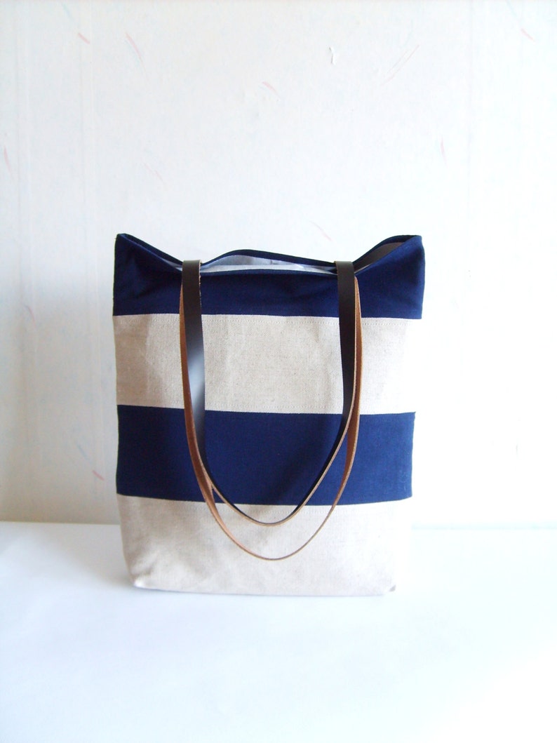 May include: A striped canvas tote bag in navy blue and beige, featuring brown leather handles. The bag's design includes horizontal stripes. It is a practical bag for carrying items, with a classic, simple style.