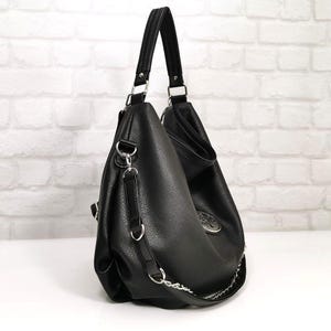 Peut inclure: Sac &agrave; bandouli&egrave;re noir avec une bandouli&egrave;re en cha&icirc;ne argent&eacute;e et une poign&eacute;e sup&eacute;rieure. Le sac a une surface textur&eacute;e et un embl&egrave;me argent&eacute; d&eacute;coratif. Le sac est en mati&egrave;re simili cuir et poss&egrave;de des accessoires argent&eacute;s.