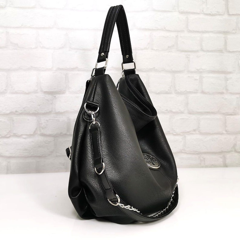 Peut inclure: Sac &agrave; bandouli&egrave;re noir avec une bandouli&egrave;re en cha&icirc;ne argent&eacute;e et une poign&eacute;e sup&eacute;rieure. Le sac a une surface textur&eacute;e et un embl&egrave;me argent&eacute; d&eacute;coratif. Le sac est en mati&egrave;re simili cuir et poss&egrave;de des accessoires argent&eacute;s.