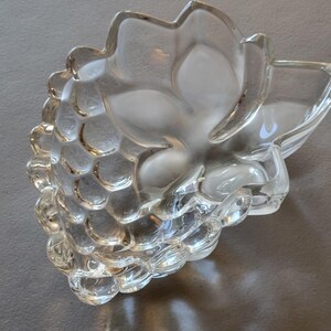 May include: A clear glass bowl shaped like a bunch of grapes. The bowl is designed with a textured surface that resembles grapes.