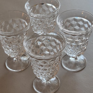 May include: Four clear, stemmed glasses with a diamond-patterned design. The glasses have a rounded bowl shape and sit on a small, circular base. The glasses are arranged on a neutral-colored surface.