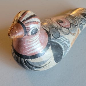 May include: Hand-painted ceramic bird figurine with black, white, gray, orange, and pink details. The bird has a long, slender body and a small beak.