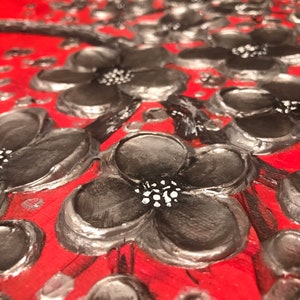 May include: Close-up of a red background with black and silver painted flowers. The flowers have a 3D effect and are painted with a textured brushstroke.