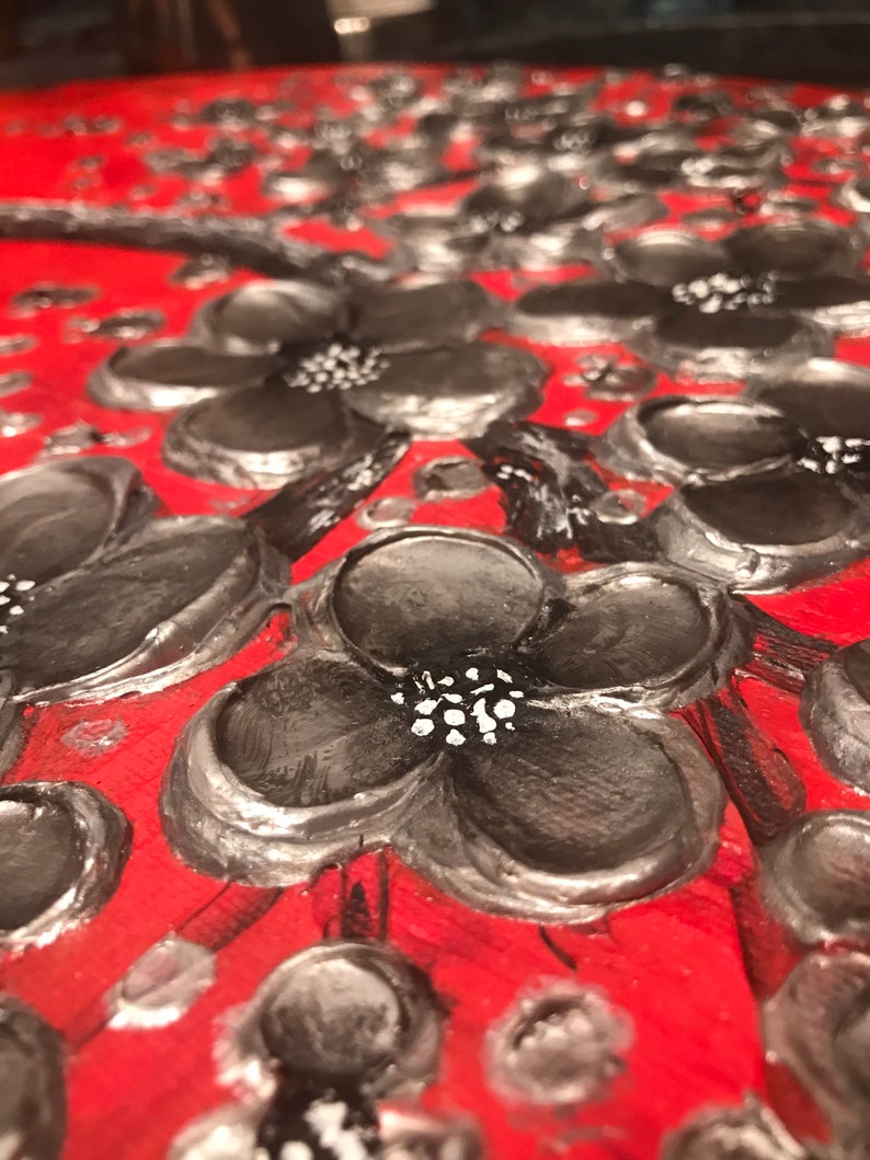 May include: Close-up of a red background with black and silver painted flowers. The flowers have a 3D effect and are painted with a textured brushstroke.