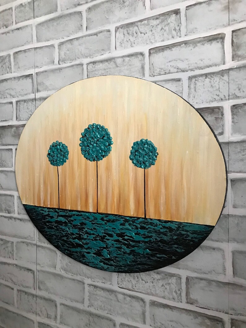 May include: A round wooden canvas painting with a teal blue water scene at the bottom and four teal blue trees in a row across the middle. The background is a light brown gradient.