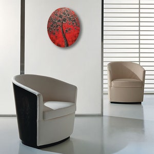 May include: A round wall art piece featuring a black tree with white flowers on a red background.