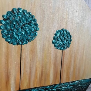 May include: A round canvas painting with a teal blue background. Two teal blue trees with textured paint stand on a brown background. The bottom of the painting is a teal blue wavy line.
