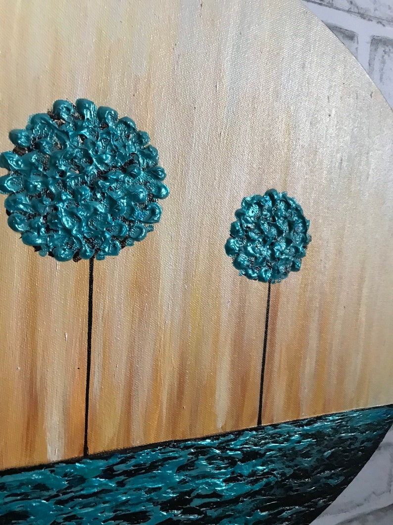 May include: A round canvas painting with a teal blue background. Two teal blue trees with textured paint stand on a brown background. The bottom of the painting is a teal blue wavy line.