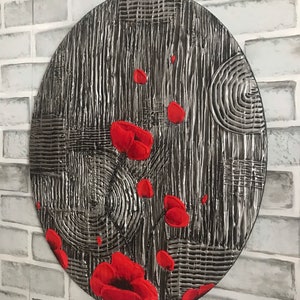 May include: Oval wall art with a textured, silver and black background. Red poppy flowers are scattered across the surface. The artwork has a unique, handcrafted appearance, adding a touch of nature-inspired decor.