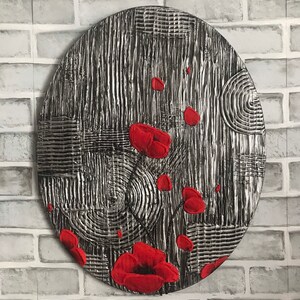May include: A round, textured wall art piece with a silver and black background. Red poppy flowers are scattered across the surface. The artwork has a modern, abstract design, perfect for home decor.