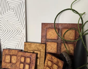 May include: A set of six square wall art pieces with a rustic, textured finish. The pieces are arranged in a staggered pattern and feature a grid of smaller squares within each larger square. The squares are a warm brown color with a hint of gold.