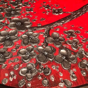 May include: A close-up of a red and black abstract painting featuring a stylized tree with silver-colored flowers. The flowers are painted in a textured style, giving the painting a three-dimensional effect.
