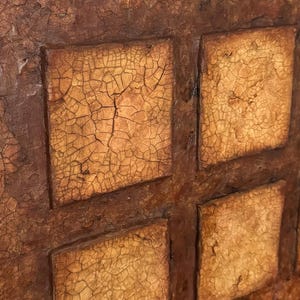 K&ouml;nnte beinhalten: Nahaufnahme einer strukturierten, braunen und gelben Wand mit einem Gittermuster. Die Wand besteht aus Quadraten mit einer rissigen, gealterten Oberfl&auml;che.