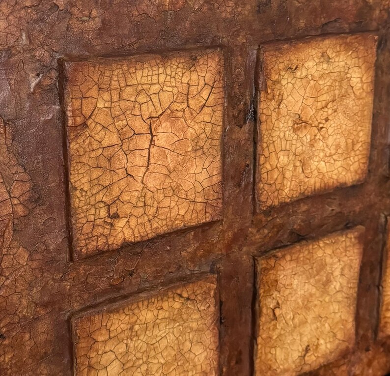K&ouml;nnte beinhalten: Nahaufnahme einer strukturierten, braunen und gelben Wand mit einem Gittermuster. Die Wand besteht aus Quadraten mit einer rissigen, gealterten Oberfl&auml;che.