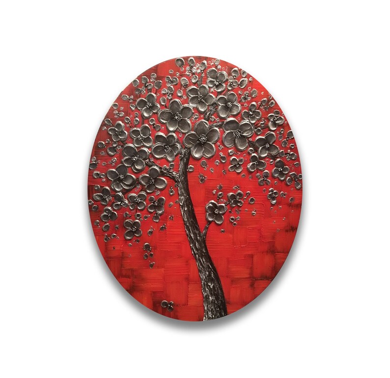 May include: A round canvas painting with a red background and a silver tree with silver flowers. The tree is in the center of the canvas and the flowers are spread out around the tree.