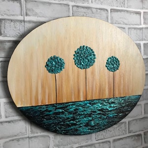 May include: A round wooden wall art piece with a teal blue water scene at the bottom and three teal blue trees with brown trunks against a light brown background.