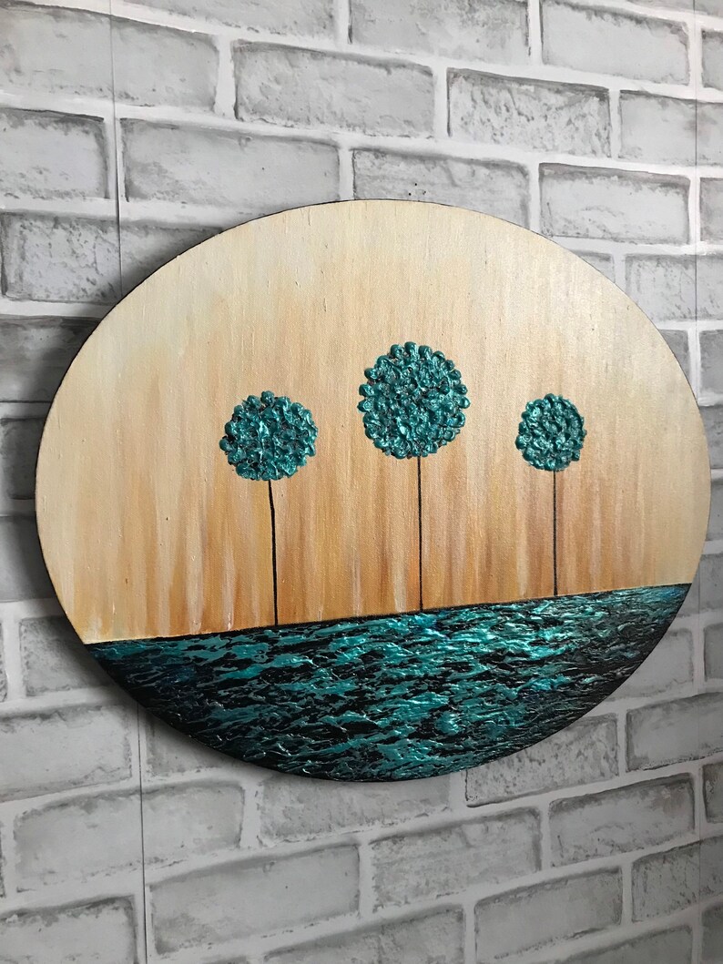 May include: A round wooden wall art piece with a teal blue water scene at the bottom and three teal blue trees with brown trunks against a light brown background.