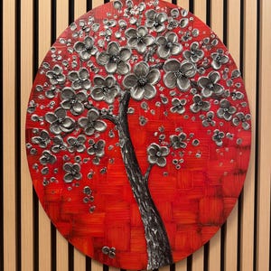 May include: A round canvas painting with a silver tree with white flowers on a red background.